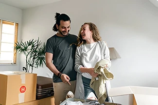 A man and woman joyfully moving boxes into a room, sharing laughter and creating a fun atmosphere during the task.