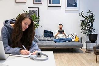 A couple sits comfortably on a couch in a cozy living room, honoring each other's space and individuality.