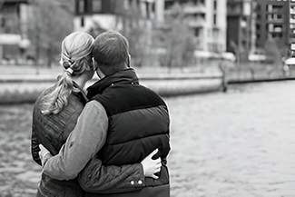 In a serene black and white scene, a couple shares a warm hug by the water, embodying appreciation and connection.