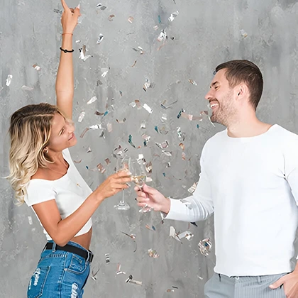 A man and woman toast with champagne glasses, surrounded by colorful confetti, celebrating their achievements together.