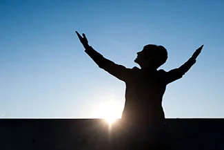 A person stands with arms outstretched towards the sun, symbolizing hope and the promise of a new beginning each day.