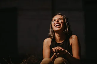 A woman laughs while sitting on the ground, her joy lighting up the moment and brightening the day.