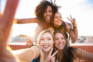 Four women smiling together as they take a selfie, capturing a joyful moment of friendship and shared happiness.