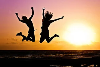 At sunset, two people leap joyfully, their happiness radiating and inspiring others to embrace joy and positivity.