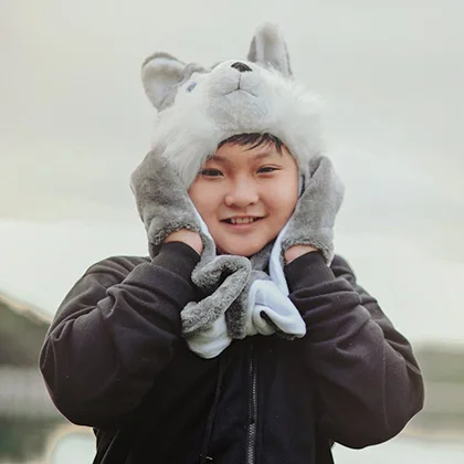 A delighted boy wearing a wolf hat enjoys the serene waterside, illustrating how happiness enriches our lives.