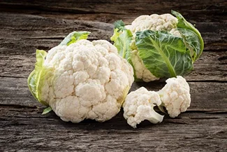 A whole cauliflower displayed on a wooden table, highlighting its vibrant green leaves and creamy white head.