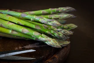 A stainless steel knife positioned next to a vibrant bunch of asparagus, highlighting the ingredients for a healthy meal.