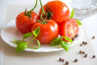 A plate of fresh tomatoes garnished with pepper and herbs, showcasing vibrant colors and a healthy presentation.