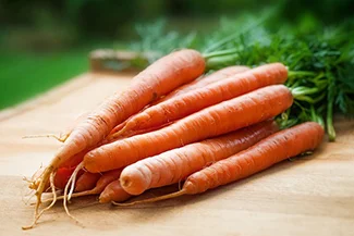 Fresh carrots neatly arranged on a wooden cutting board, ready for preparation in a culinary setting.