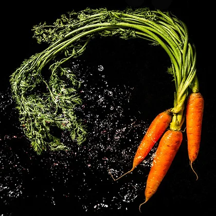 A vibrant bunch of fresh carrots with green tops, arranged neatly on a wooden surface, showcasing their rich orange color.