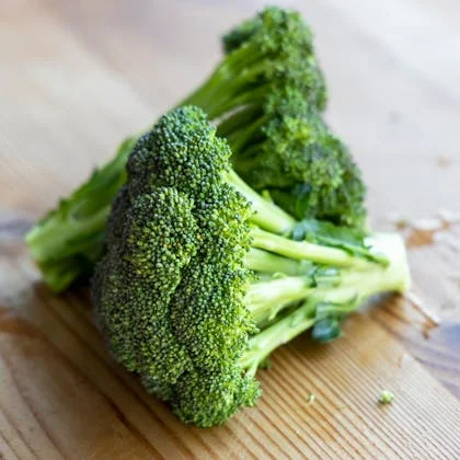 A fresh piece of broccoli placed on a wooden table, highlighting its rich green hue and natural form against the wood.