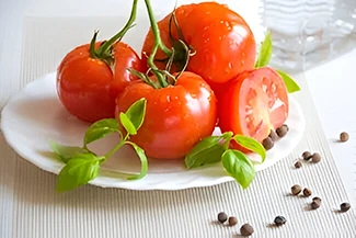 A plate of fresh tomatoes garnished with pepper and herbs, showcasing vibrant colors and a healthy presentation.