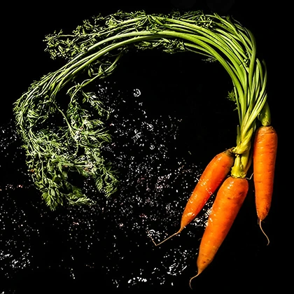 A vibrant bunch of fresh carrots with green tops, arranged neatly on a wooden surface, showcasing their rich orange color.