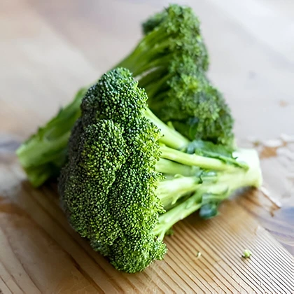A fresh piece of broccoli placed on a wooden table, highlighting its rich green hue and natural form against the wood.