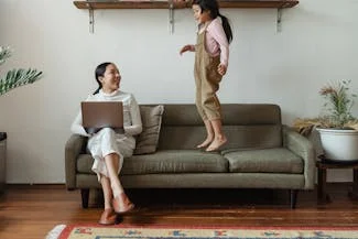 A woman and child sit together on a couch, using a laptop, exemplifying the balance of work and family life.