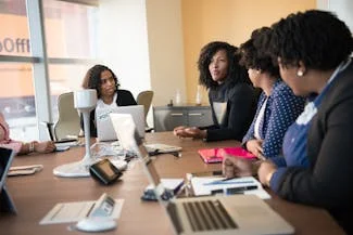 A diverse group of women engaged in discussion around a conference table, showcasing their strong communication skills.