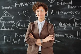 A woman stands confidently in front of a chalkboard filled with math formulas, symbolizing women's growing presence in higher education.