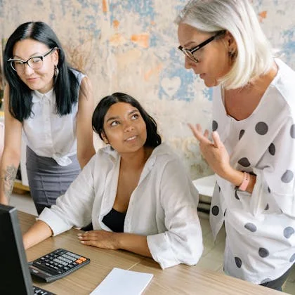 Three professional women in business attire engage with a computer screen, exemplifying their effective communication abilities.