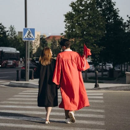 Two graduates in gowns crossing the street, representing the increasing pursuit of higher education by women today.